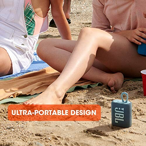 People on a beach with a portable JBL speaker.