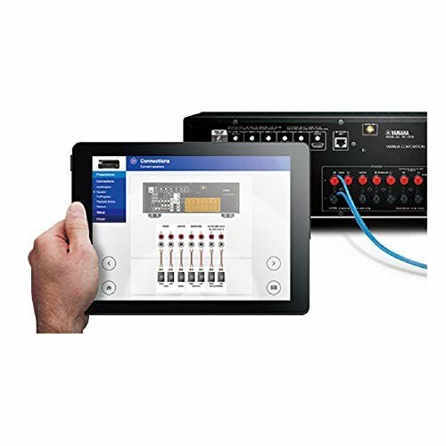 Hand holding a tablet showing an audio mixer interface, with a mixer device in the background.