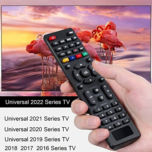 Hand holding a universal TV remote control in front of a television displaying flamingos.